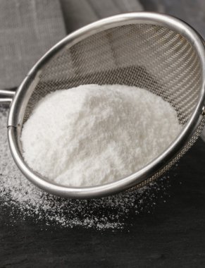 gri bir arka plan üzerinde metal bir süzgeç içinde toz şeker