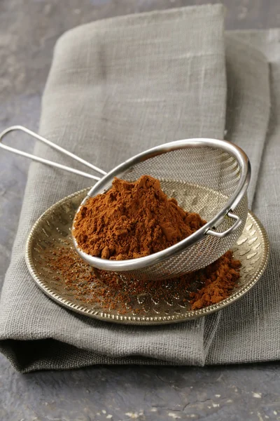 Cocoa powder in a metal sieve with a gray background — Stock Photo, Image