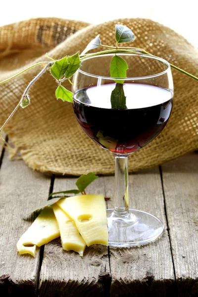 Copo de vinho tinto e fatias de queijo em uma mesa de madeira — Fotografia de Stock