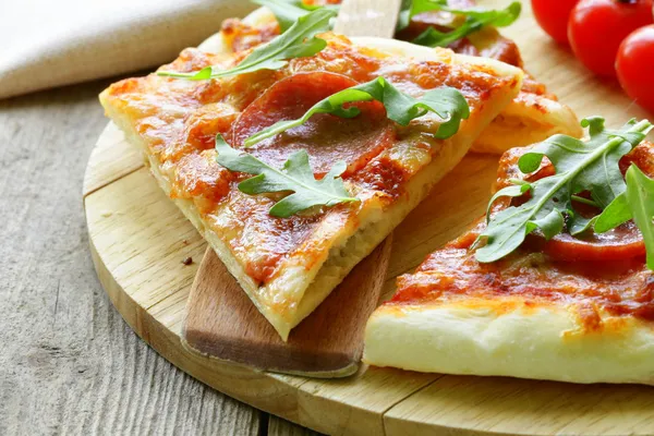 Pepperoni pizza with tomato sauce and herbs on a wooden board — Stock Photo, Image