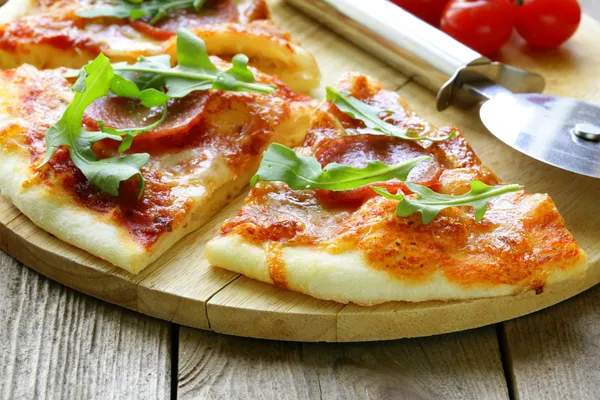 Pepperoni pizza with tomato sauce and herbs on a wooden board — Stock Photo, Image