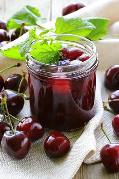 Cherry jam v sklenice a zralé bobule na stůl — Stock fotografie