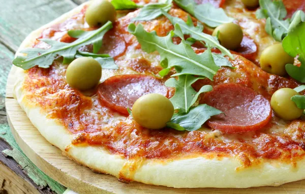 Pizza al salame piccante con salsa di pomodoro ed erbe aromatiche su una tavola di legno — Foto Stock