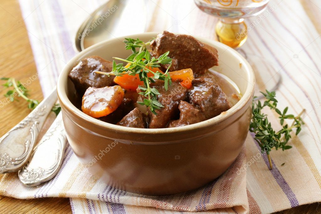 Beef goulash (stew) with vegetables and herbs on a wooden table