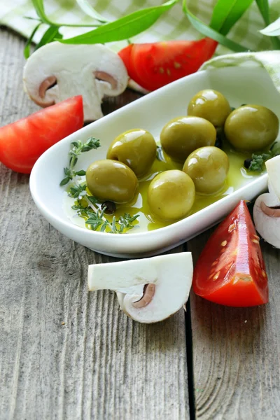 Зеленые оливки с овощами (помидоры и грибы) на деревянном столе — стоковое фото