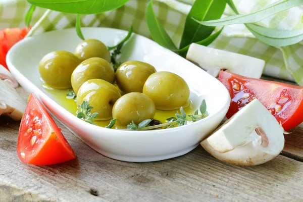 Zielone oliwki z warzywami (pomidor i grzyby) na drewnianym stołem — Zdjęcie stockowe