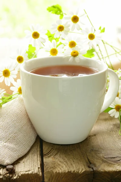 Tasse Tee und Kamillenblüten auf einem Holztisch — Stockfoto