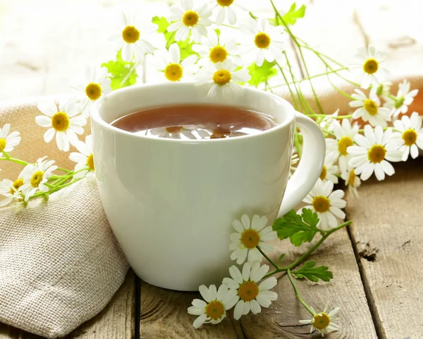 Kopje thee en kamille bloemen op een houten tafel — Stockfoto