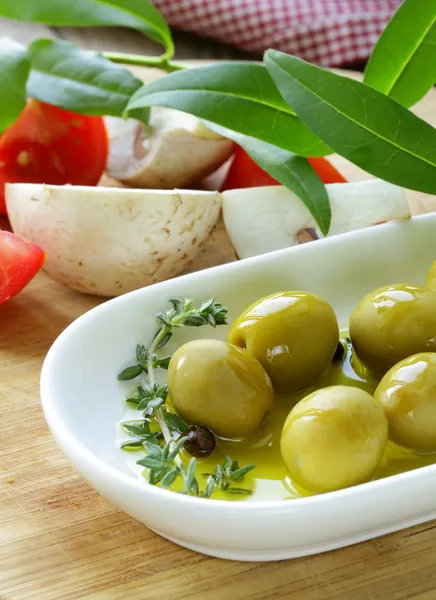 Green olives with vegetables (tomato and mushrooms) on a wooden table — Stock Photo, Image