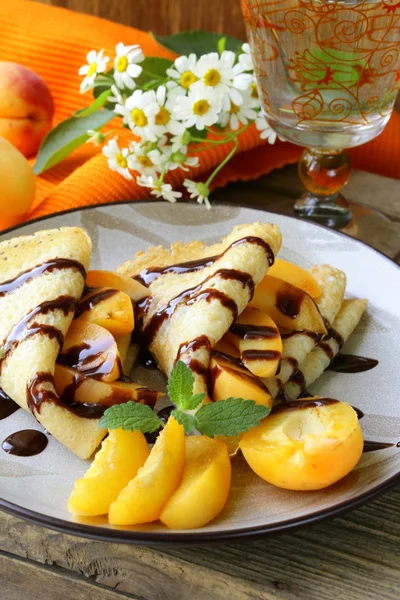 Thin pancakes (crepes) with peaches and chocolate sauce — Stock Photo, Image