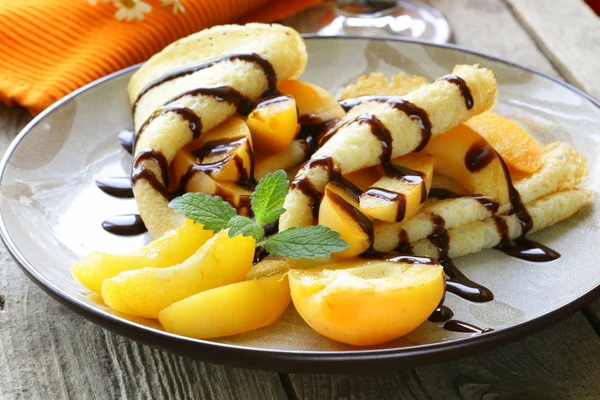 Thin pancakes (crepes) with peaches and chocolate sauce — Stock Photo, Image