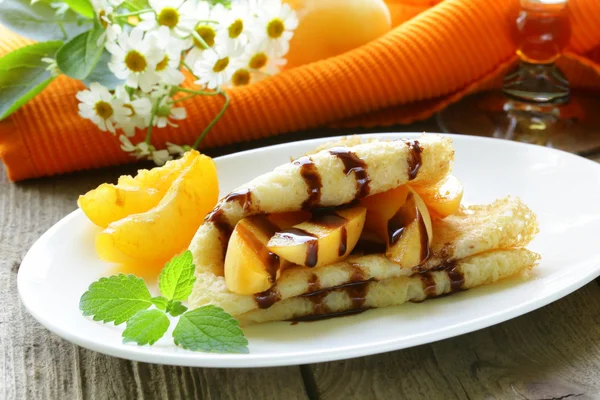 Thin pancakes (crepes) with peaches and chocolate sauce — Stock Photo, Image