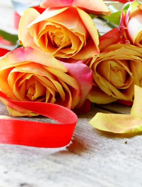 Ramo de rosas naranjas y cinta roja sobre una mesa de madera —  Fotos de Stock