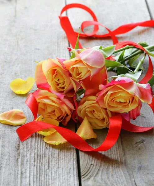 Ramo de rosas naranjas y cinta roja sobre una mesa de madera —  Fotos de Stock