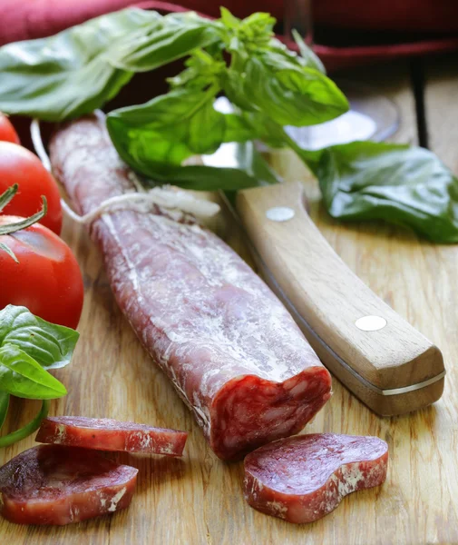 Still life of delicacy salami, tomatoes and basil - rustic style — Stock Photo, Image