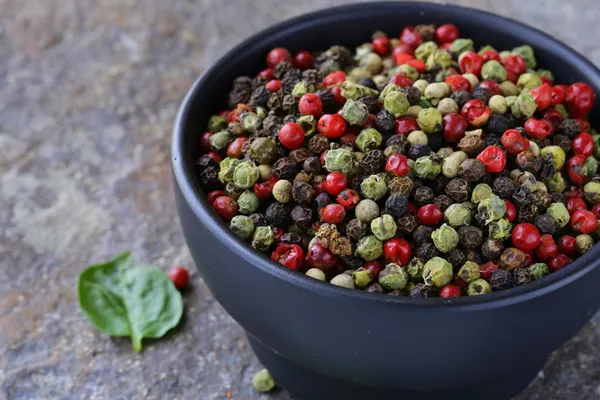 Verschiedene rote, schwarze und grüne Paprika in einer Schüssel auf dem Tisch — Stockfoto