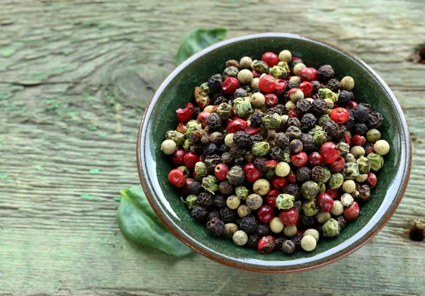 Verschiedene rote, schwarze und grüne Paprika in einer Schüssel auf dem Tisch — Stockfoto