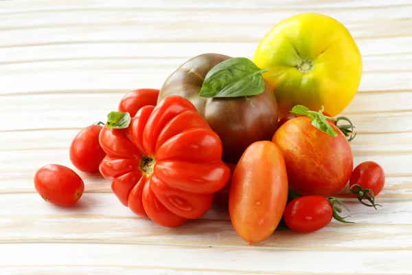 Different varieties of tomato with basil on a wooden table — Stock Photo, Image