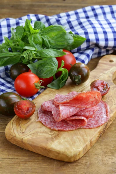 Gerookte worst, tomaten en basilicum op een houten snijplank — Stockfoto