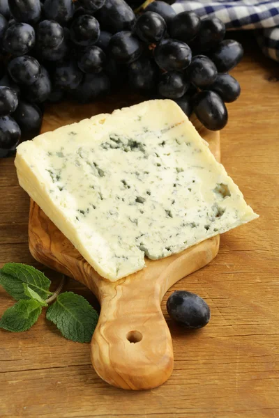 Pedazo de queso azul con uvas en una tabla de madera — Foto de Stock