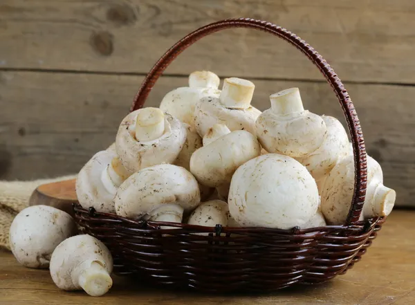 Ekologické houby (žampiony) v koši na dřevěné pozadí — Stock fotografie