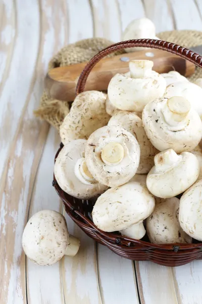 Organic mushrooms (champignons) in a basket on a wooden background — Stock Photo, Image