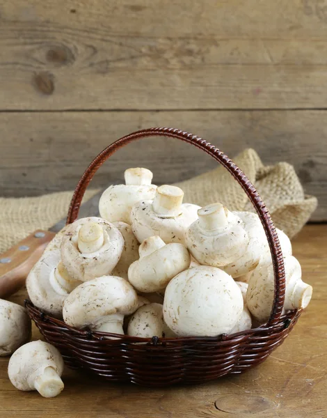 Cogumelos orgânicos (champinhons) em uma cesta em um fundo de madeira — Fotografia de Stock