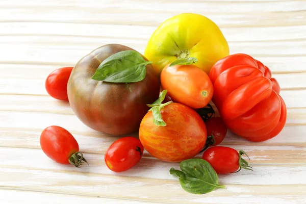 Different varieties of tomato with basil on a wooden table — Stock Photo, Image