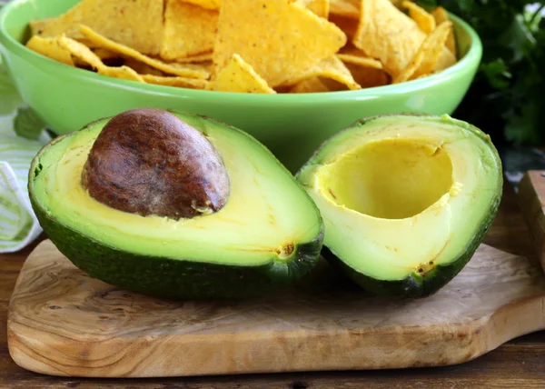 Avocado on a wooden table and corn chips in the background — Stock Photo, Image