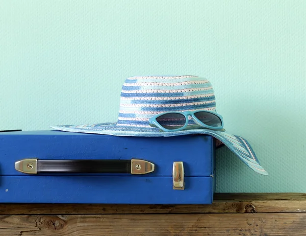 Old fashioned blue suitcase for travel and beach hat on a turquoise background — Stock Photo, Image