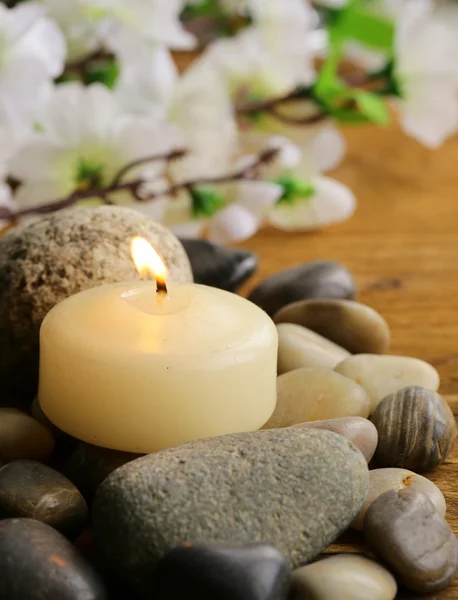 Bodegón una vela encendida y piedras sobre fondo de madera Imagen De Stock