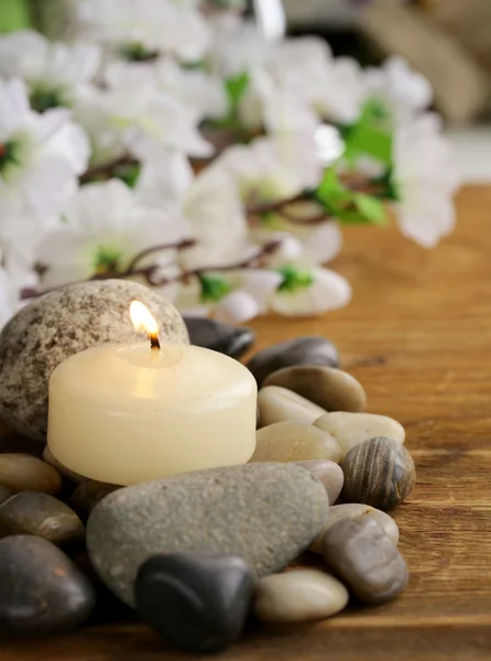 Still life a lit candle and stones on wooden background Royalty Free Stock Photos
