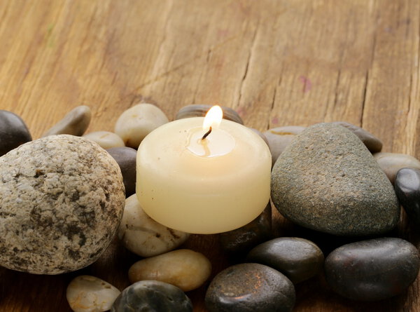 Still life a lit candle and stones on wooden background