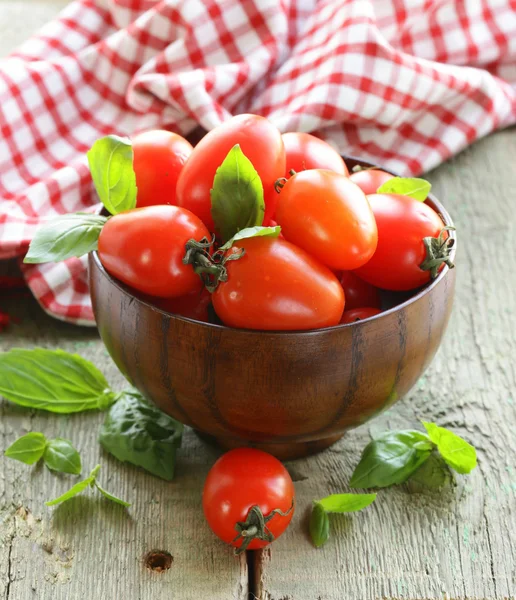 Tomates cereja com folhas de manjericão em uma tigela de madeira — Fotografia de Stock