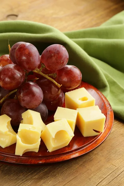 Wooden plate with cheese (Maasdam) and red grapes — Stock Photo, Image