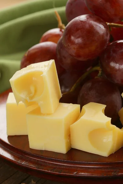 Wooden plate with cheese (Maasdam) and red grapes — Stock Photo, Image