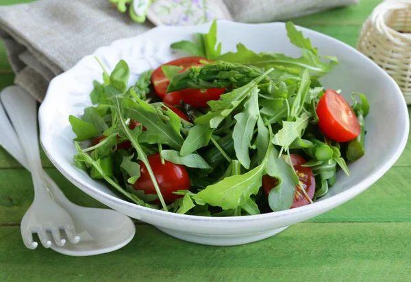 Salad with arugula and tomatoes served on a wooden table — Stock Photo, Image