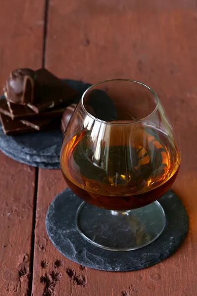 Vaso de brandy con chocolate sobre mesa de madera —  Fotos de Stock