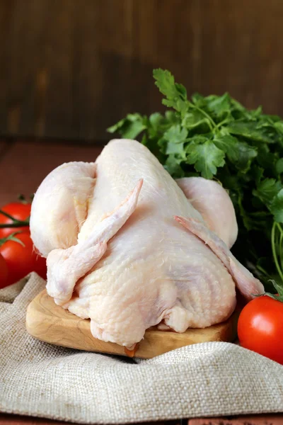 Pollo crudo fresco en una tabla de cortar con verduras y hierbas —  Fotos de Stock