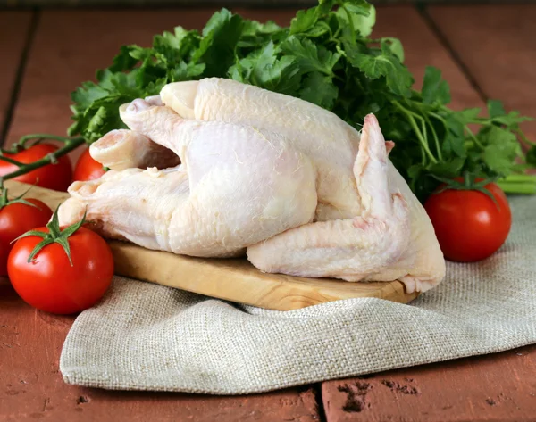 Pollo crudo fresco en una tabla de cortar con verduras y hierbas —  Fotos de Stock