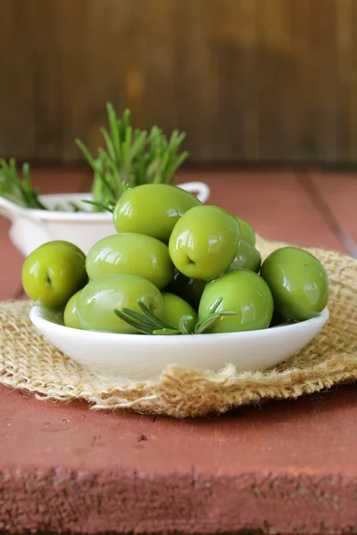 Zelené olivy marinované v misce na dřevěný stůl — Stock fotografie
