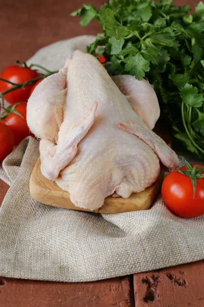Pollo crudo fresco en una tabla de cortar con verduras y hierbas —  Fotos de Stock