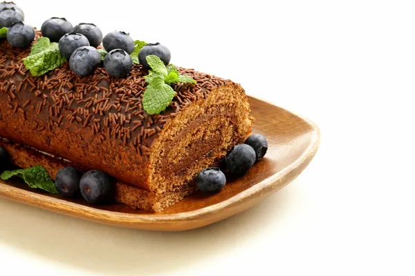 Chocolate biscuit roll garnished with mint leaves and blueberries — Stock Photo, Image