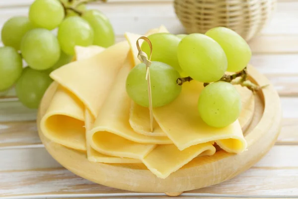 Käse auf einem Holzbrett mit grünen Trauben serviert — Stockfoto