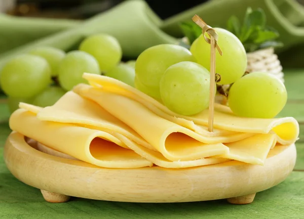 Queijo servido em uma tábua de madeira com uvas verdes — Fotografia de Stock