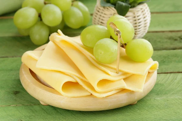 Queijo servido em uma tábua de madeira com uvas verdes — Fotografia de Stock