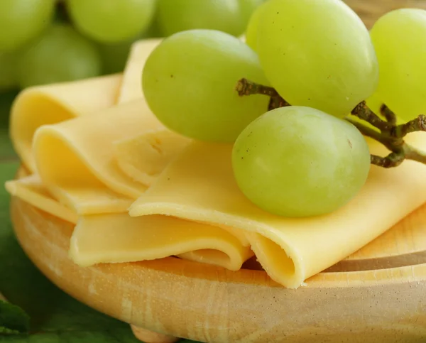 Käse auf einem Holzbrett mit grünen Trauben serviert — Stockfoto