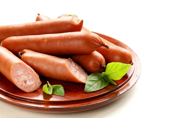 Deliziose salsicce affumicate su un piatto di legno con foglie di basilico — Foto Stock