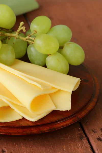 Queijo servido em uma tábua de madeira com uvas verdes — Fotografia de Stock