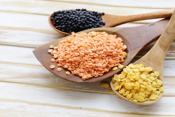 Diferentes tipos de lentilhas - vermelho, amarelo e preto em colheres de madeira — Fotografia de Stock